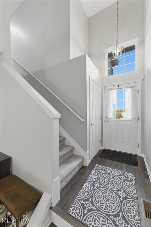 Entrance foyer with a towering ceiling, stairs, dark wood finished floors, and a chandelier