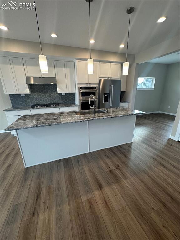 Kitchen featuring white cabinets, decorative light fixtures, tasteful backsplash, dark wood finished floors, and dark stone countertops