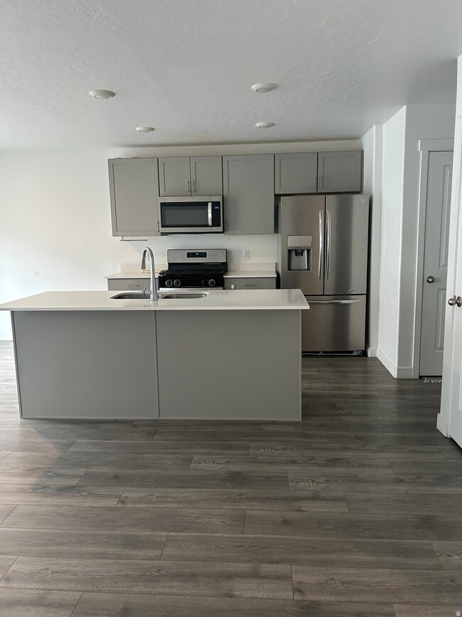 Kitchen with gray cabinetry, stainless steel appliances, a center island with sink, a textured ceiling, and dark laminate finished floors