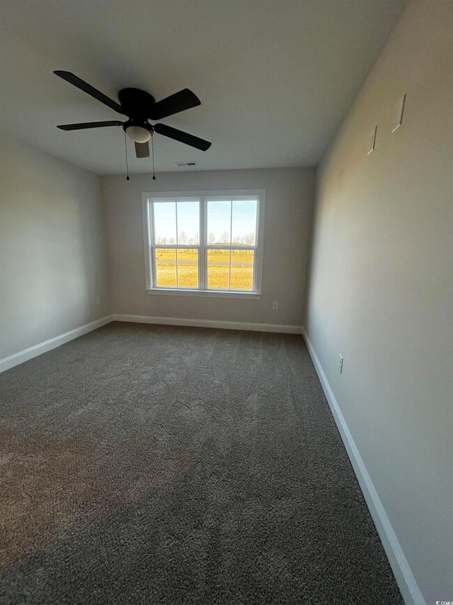Carpeted empty room featuring a ceiling fan, baseb
