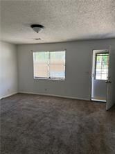 Unfurnished room with dark colored carpet and a textured ceiling
