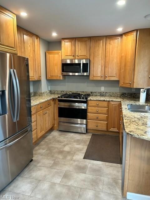 Kitchen featuring stainless steel gas range, sink, light tile floors, light stone countertops, and fridge
