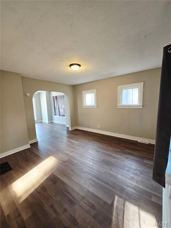 Spare room featuring arched walkways, dark wood-style flooring, and a textured ceiling
