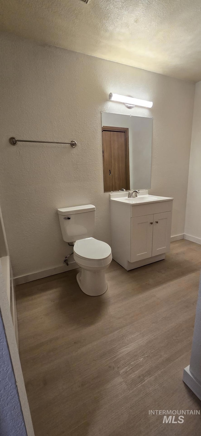 Half bathroom featuring a textured wall, vanity, light wood-style floors, and a textured ceiling