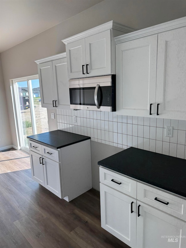 Kitchen featuring dark countertops, stainless steel microwave, white cabinets, and dark wood-style flooring