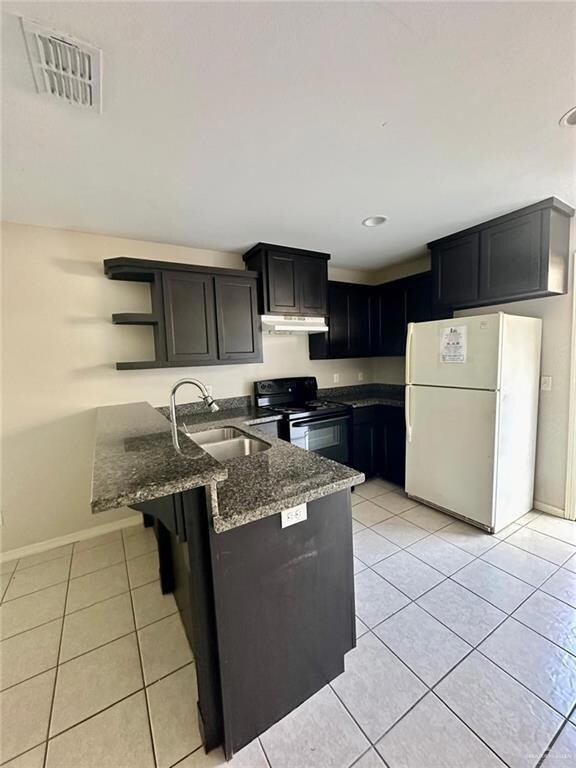 Kitchen featuring white fridge, black electric range oven, light tile patterned floors, dark stone counters, and sink