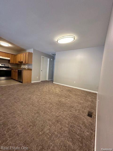 Unfurnished living room/dining room featuring dark colored carpet and baseboards