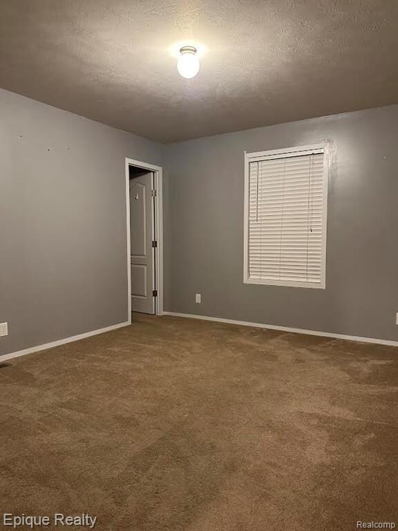 Carpeted spare room featuring a textured ceiling and baseboards