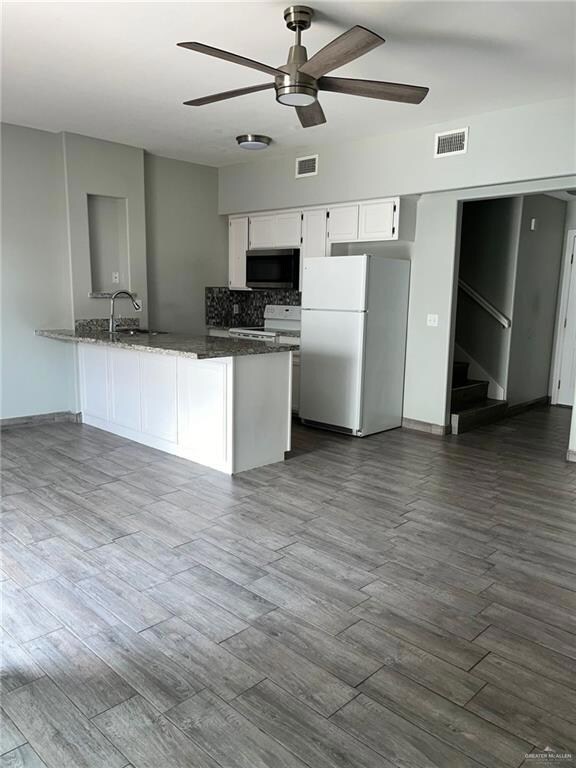 Kitchen with white cabinets, white appliances, a peninsula, dark wood finished floors, and ceiling fan