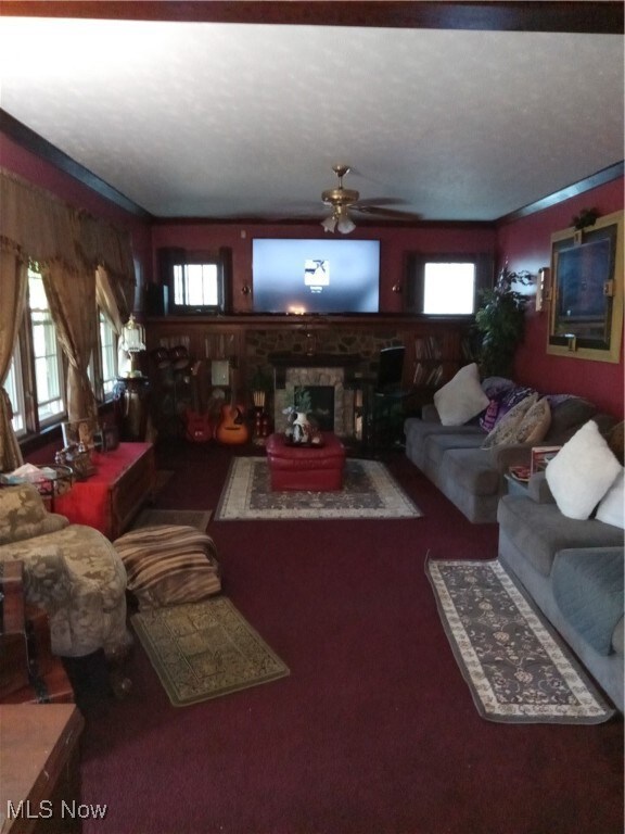 Living room with ceiling fan, a wealth of natural light, crown molding, and a stone fireplace