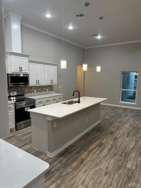 Kitchen with ornamental molding, a kitchen island with sink, visible vents, stove, and a sink