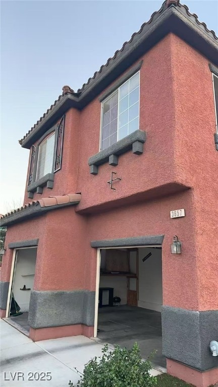 View of side of property with an attached garage, stucco siding, and a tiled roof