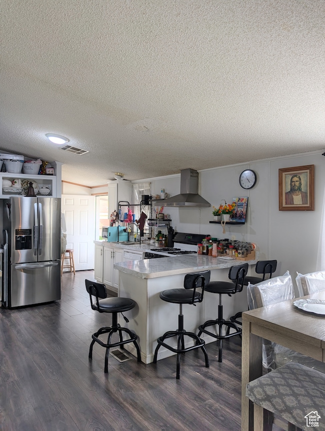 Kitchen featuring stainless steel fridge with ice dispenser, dark wood finished floors, a peninsula, a kitchen breakfast bar, and a textured ceiling