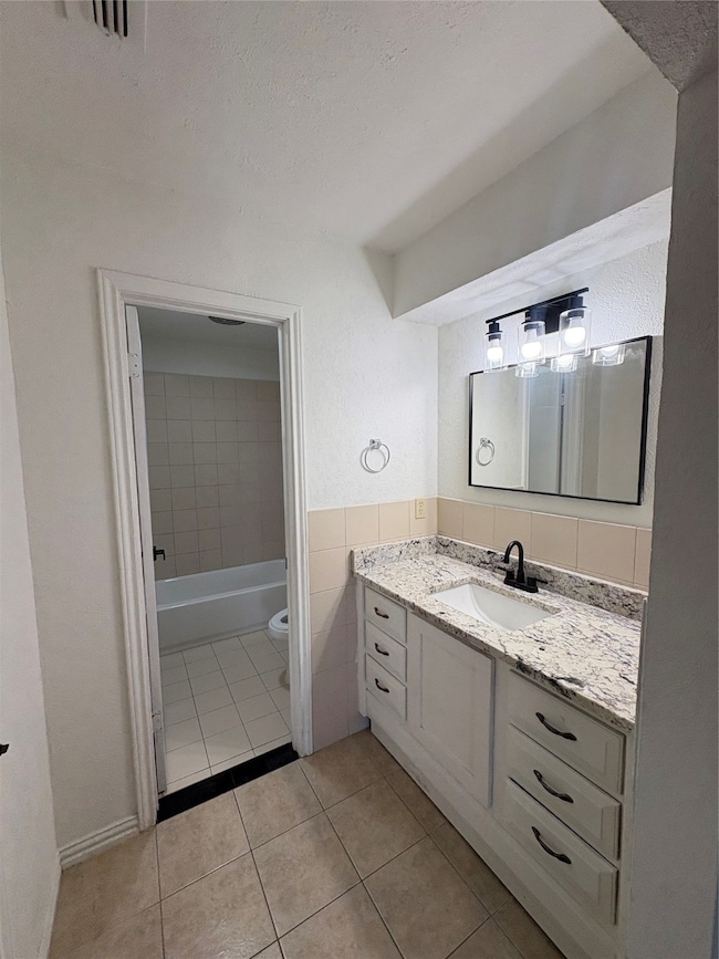 Bathroom featuring vanity, light tile patterned flooring, a textured ceiling, and  shower combination