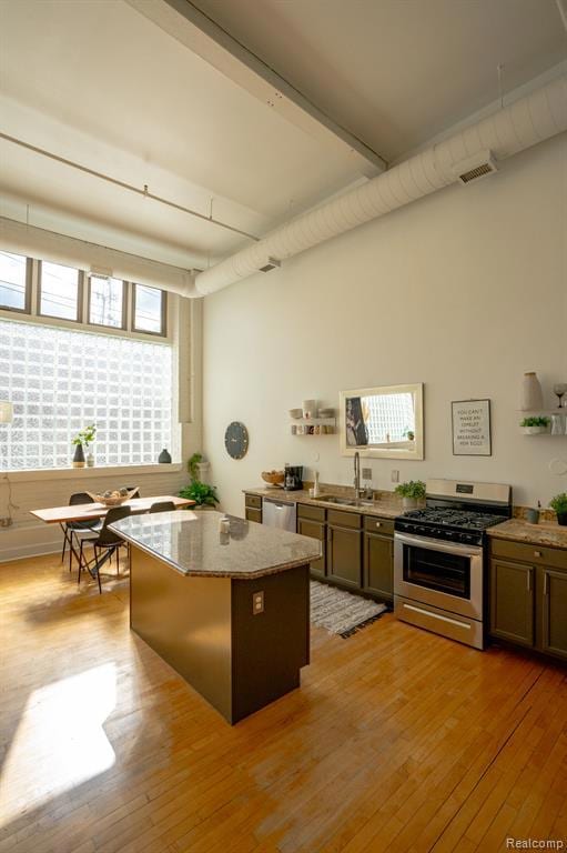 Kitchen with appliances with stainless steel finishes, light stone counters, light wood-type flooring, and a kitchen island