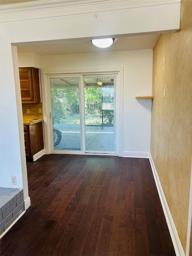 Unfurnished dining area featuring dark wood-style flooring and baseboards