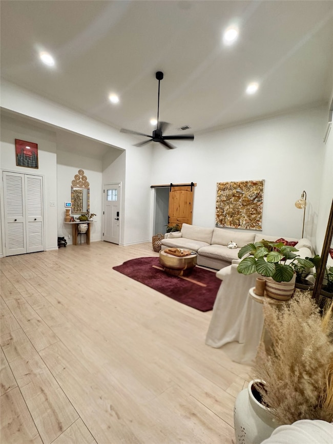 Living area with a barn door, light wood-style floors, recessed lighting, and a ceiling fan