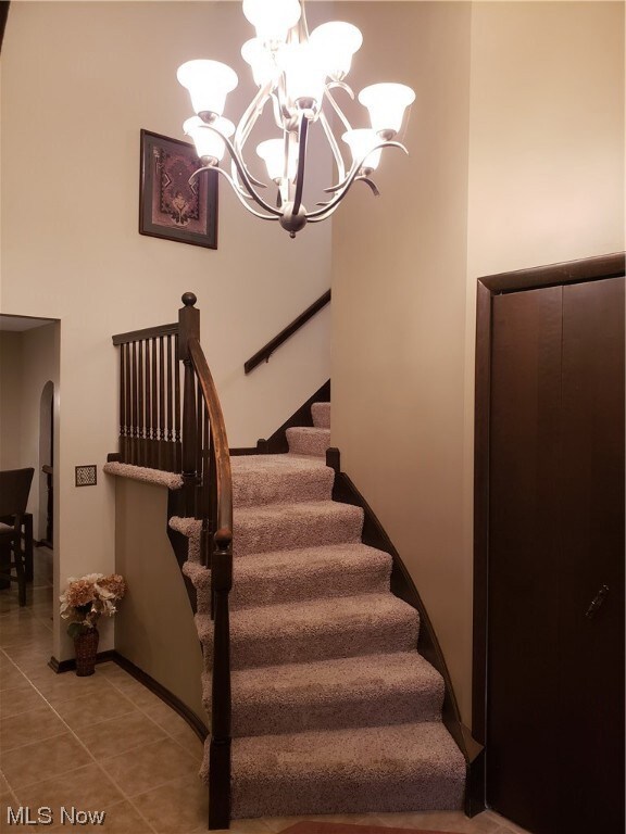 Stairs with an inviting chandelier and light tile floors