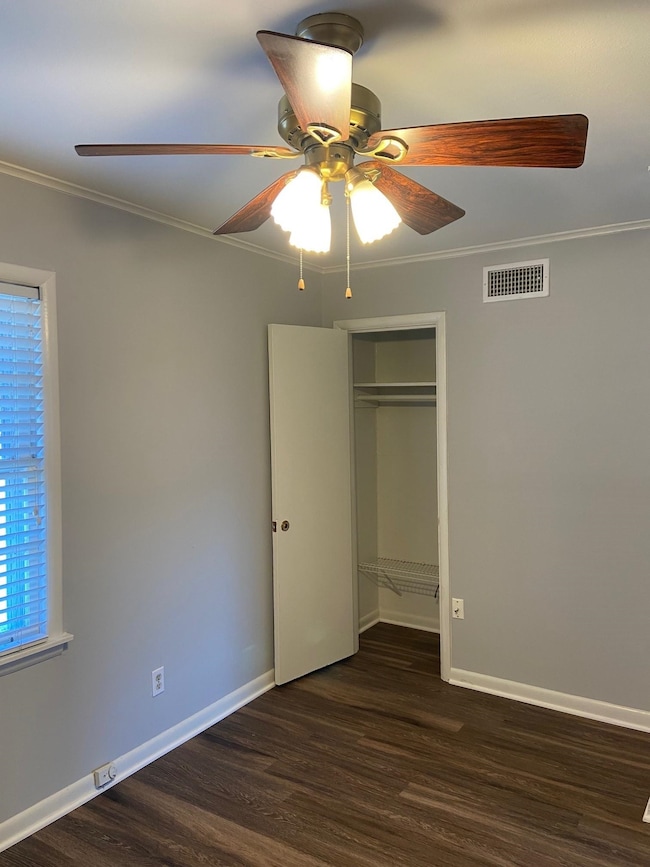 Unfurnished bedroom featuring crown molding, wood finished floors, baseboards, a ceiling fan, and a closet