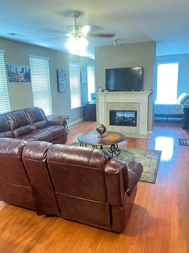 Living area featuring a ceiling fan, a tiled fireplace, wood finished floors, and baseboards