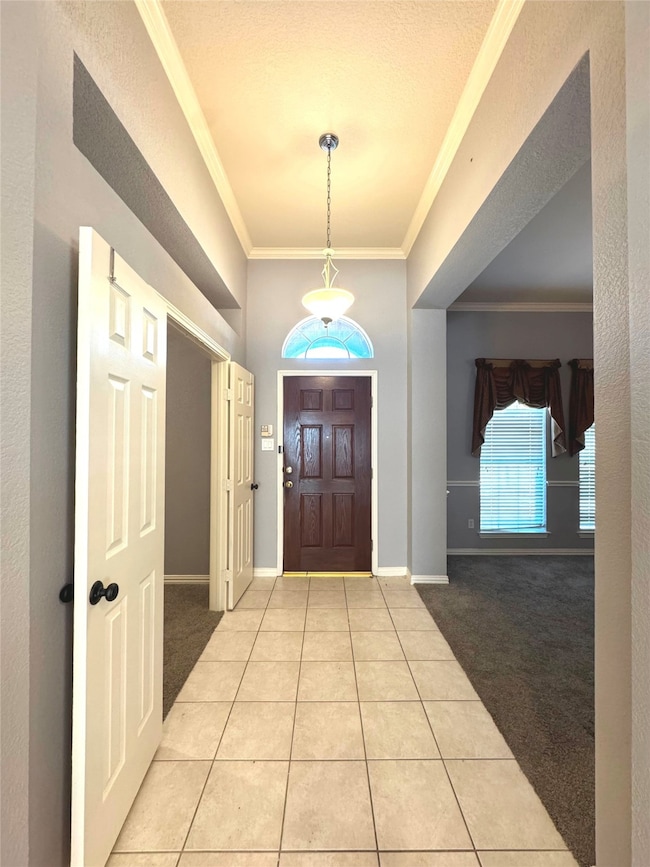 Entryway featuring light colored carpet, light tile patterned flooring, and ornamental molding
