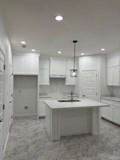 Kitchen featuring white cabinets, a center island with sink, and light tile floors