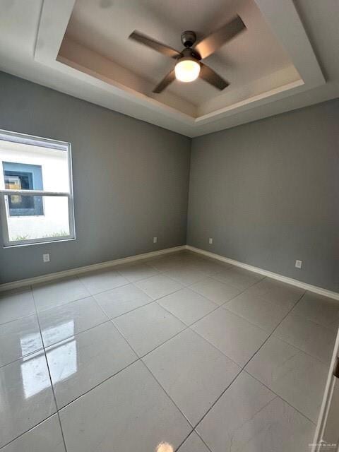 Spare room with a tray ceiling, a ceiling fan, and tile patterned flooring