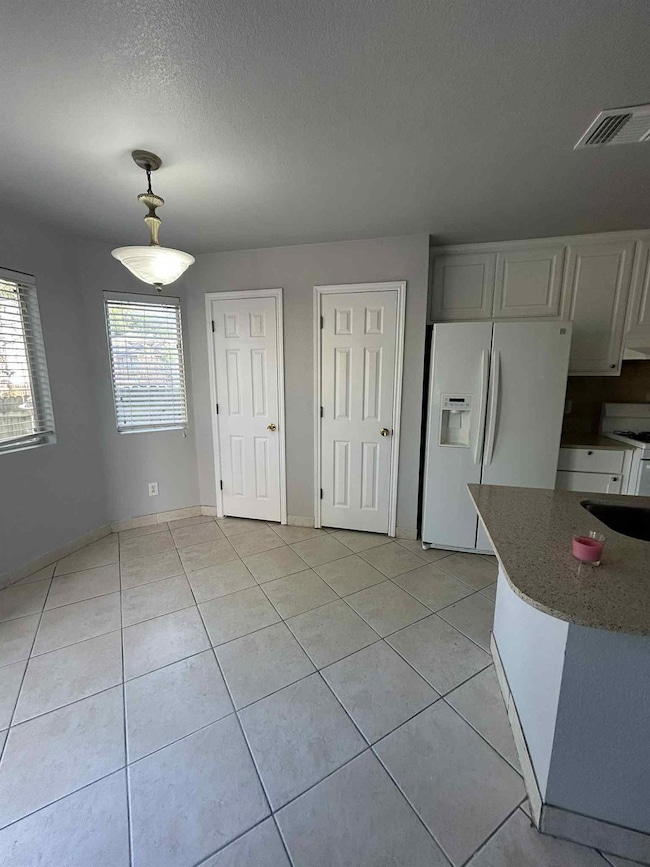Kitchen with light stone counters, white appliances, light tile patterned flooring, a textured ceiling, and white cabinets