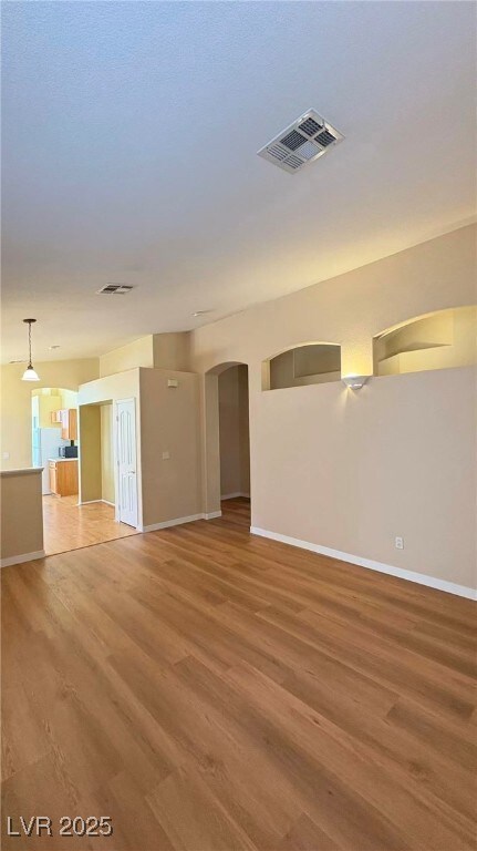 Unfurnished living room with arched walkways and light wood-style flooring