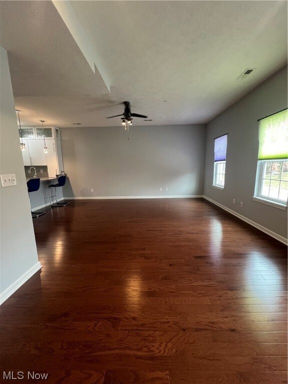 Unfurnished living room with dark hardwood / wood-style flooring, ceiling fan, and a textured ceiling
