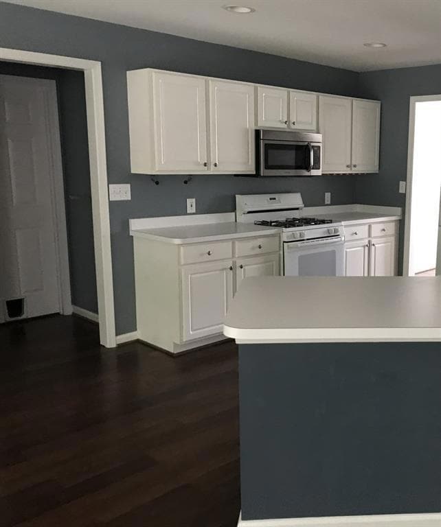 Kitchen featuring stainless steel microwave, gas range gas stove, light countertops, dark wood-style floors, and white cabinetry