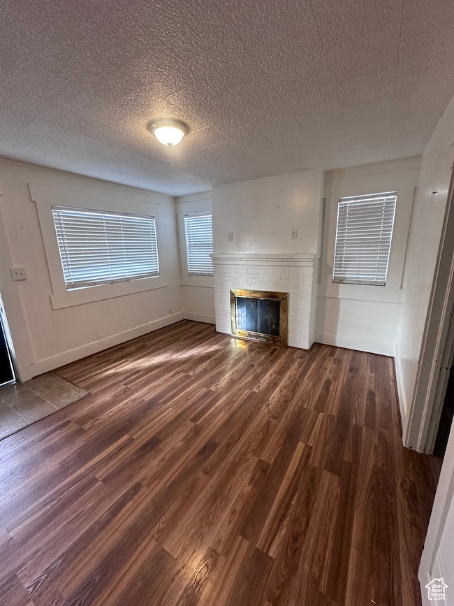 Unfurnished living room with dark hardwood / wood-style flooring, a fireplace, and a textured ceiling