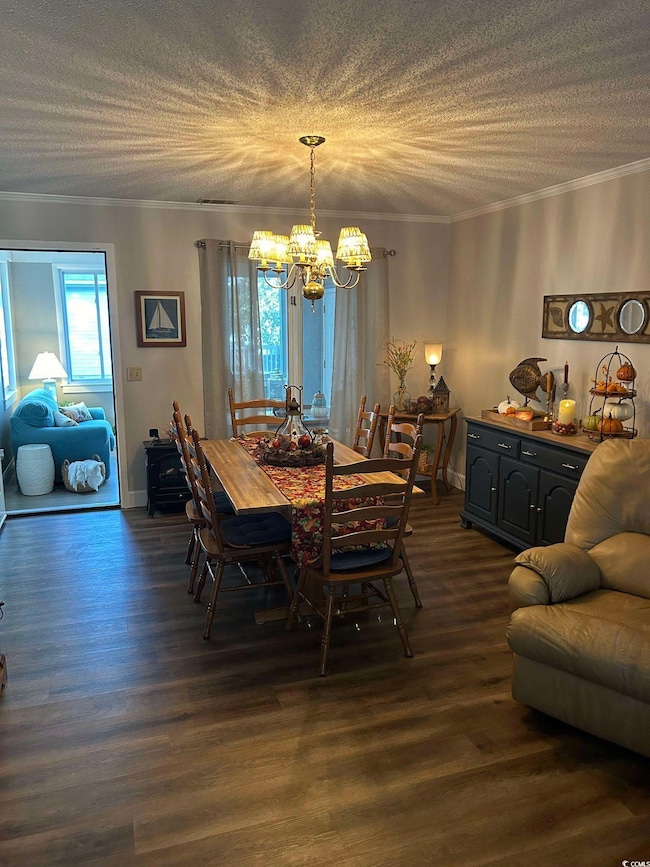 Dining room featuring a chandelier, crown molding, dark wood-style floors, and a textured ceiling