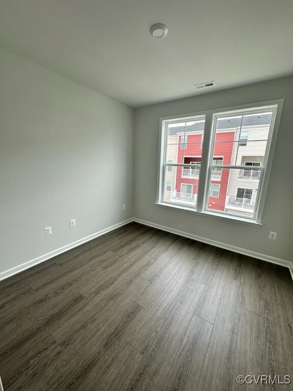 Spare room with baseboards, plenty of natural light, dark wood-style floors, and visible vents