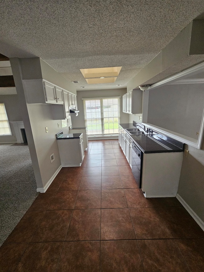 Kitchen featuring a textured ceiling, stainless steel dishwasher, white cabinets, dark tile patterned flooring, and dark countertops