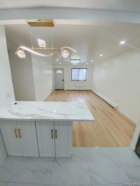 Kitchen with white cabinetry, light stone counters, open floor plan, a baseboard heating unit, and recessed lighting