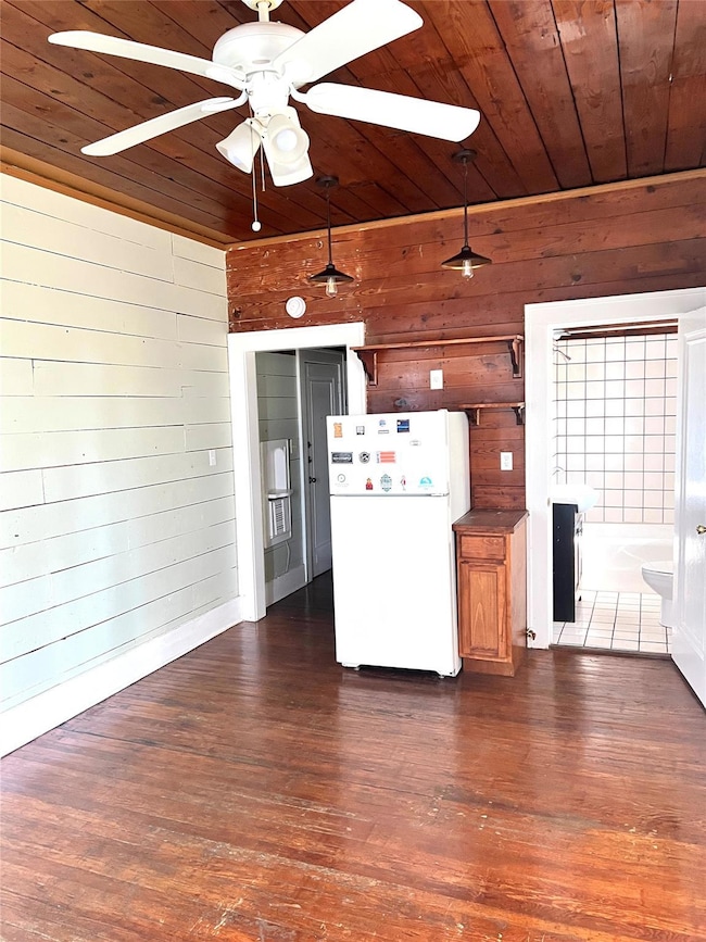 Kitchen featuring wooden walls, freestanding refrigerator, wood ceiling, dark wood finished floors, and hanging light fixtures