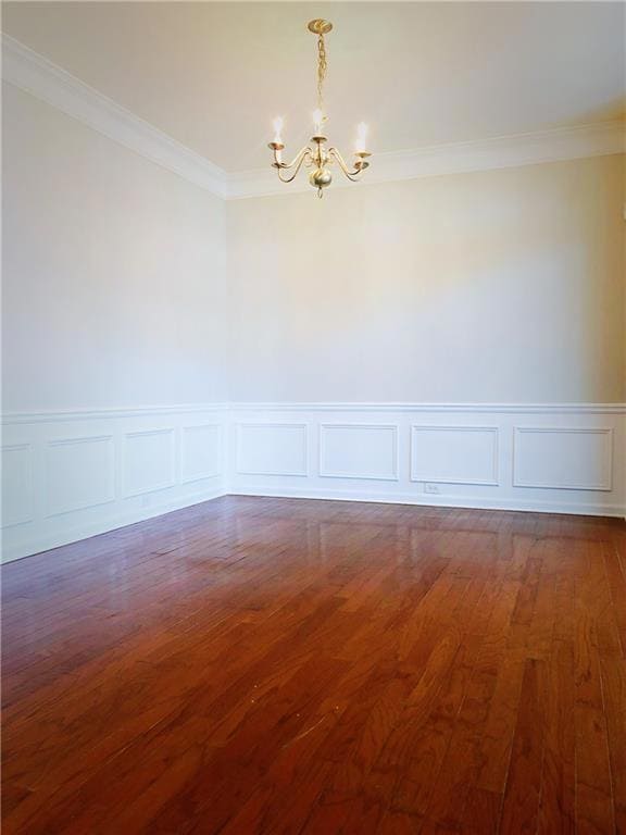 Empty room with a chandelier, a decorative wall, dark wood-style flooring, a wainscoted wall, and ornamental molding
