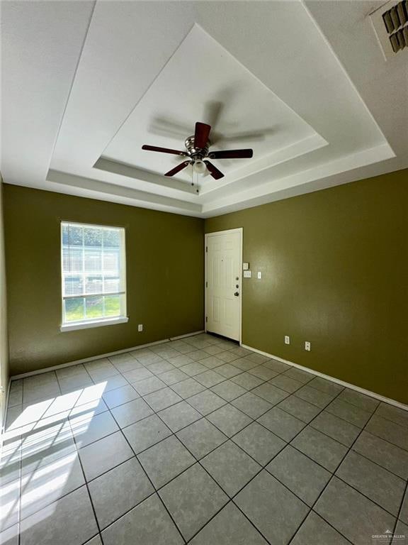 Unfurnished room with a raised ceiling, light tile patterned floors, and a ceiling fan