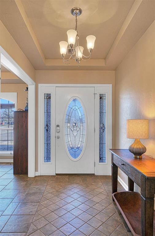 Foyer with a chandelier, a tray ceiling, and tile 