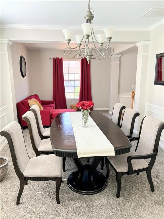Dining area with a chandelier, ornamental molding, decorative columns, and carpet