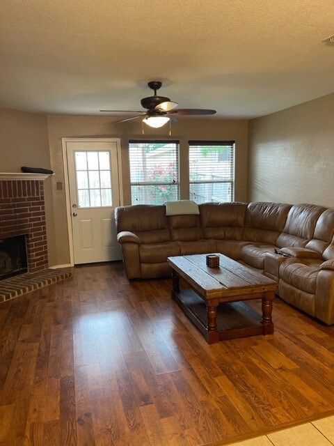 Living room featuring plenty of natural light, a ceiling fan, a brick fireplace, and wood finished floors