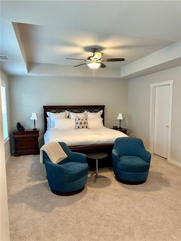 Carpeted bedroom with ceiling fan and a tray ceili
