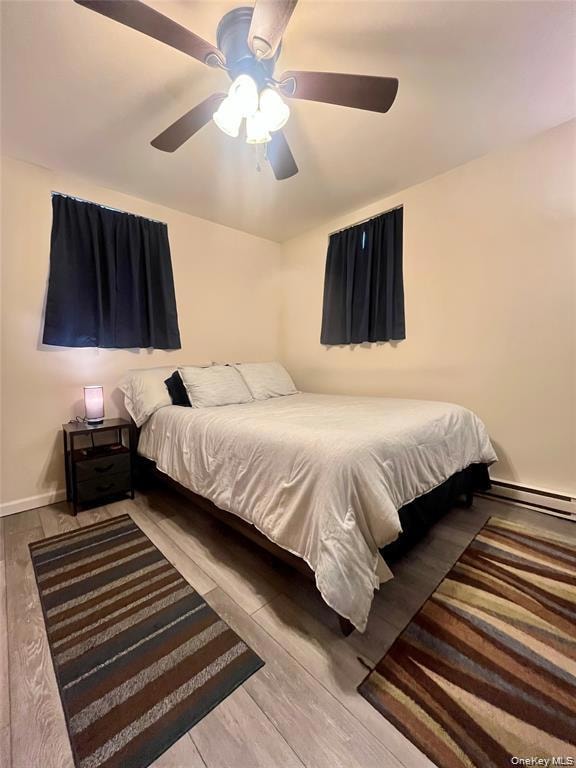 Bedroom featuring a ceiling fan, baseboard heating, and light wood-style floors