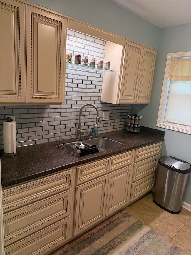 Kitchen with cream cabinets, a sink, decorative backsplash, and dark countertops