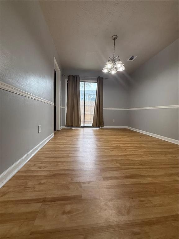 Empty room featuring light wood finished floors, a chandelier, and a textured ceiling