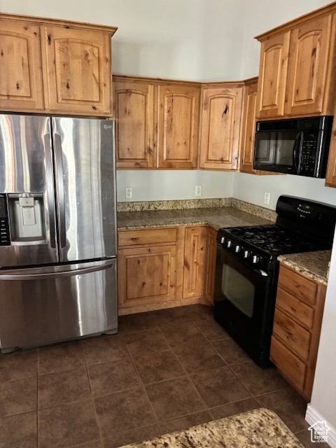 Kitchen featuring black appliances, dark stone counters, dark tile patterned flooring, and brown cabinetry