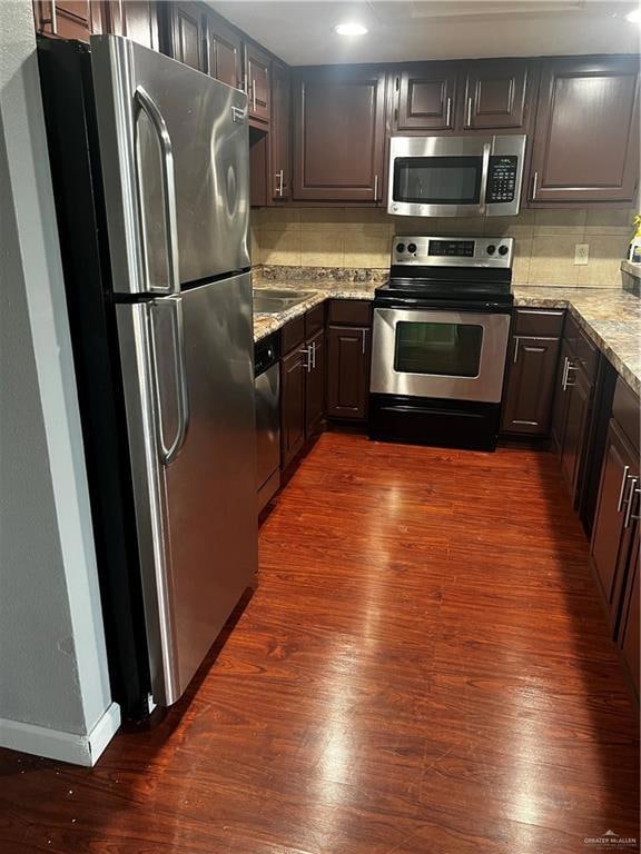 Kitchen featuring dark wood finished floors, fridge, dishwashing machine, light stone countertops, and stove