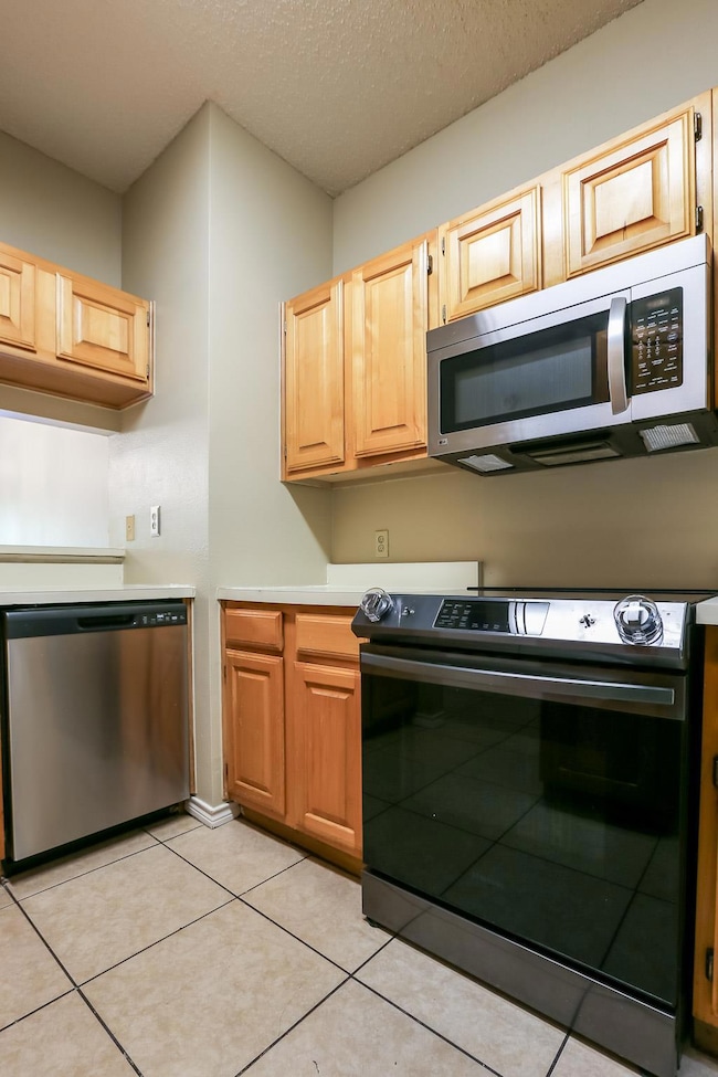 Kitchen with stainless steel appliances, light countertops, light tile patterned floors, and light brown cabinets