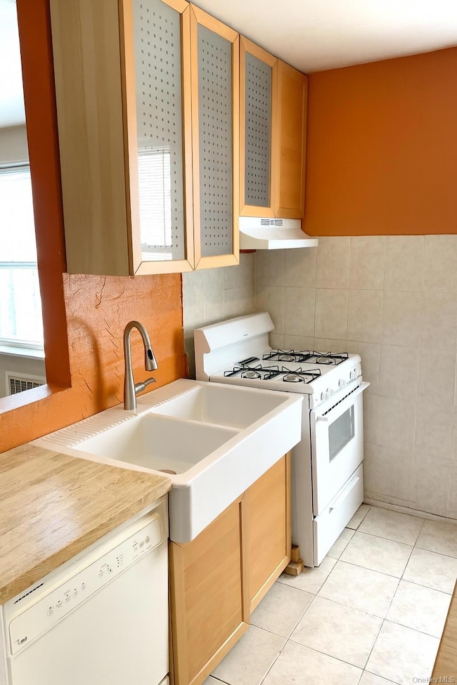 Kitchen featuring white appliances, light countertops, tasteful backsplash, light tile patterned floors, and tile walls. AI enhanced.